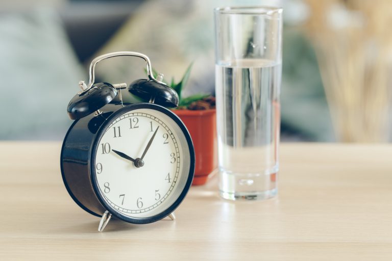 Vaso de agua junto a un reloj, representando la importancia de los pequeños cambios en casa para ahorrar agua y promover un estilo de vida sostenible.