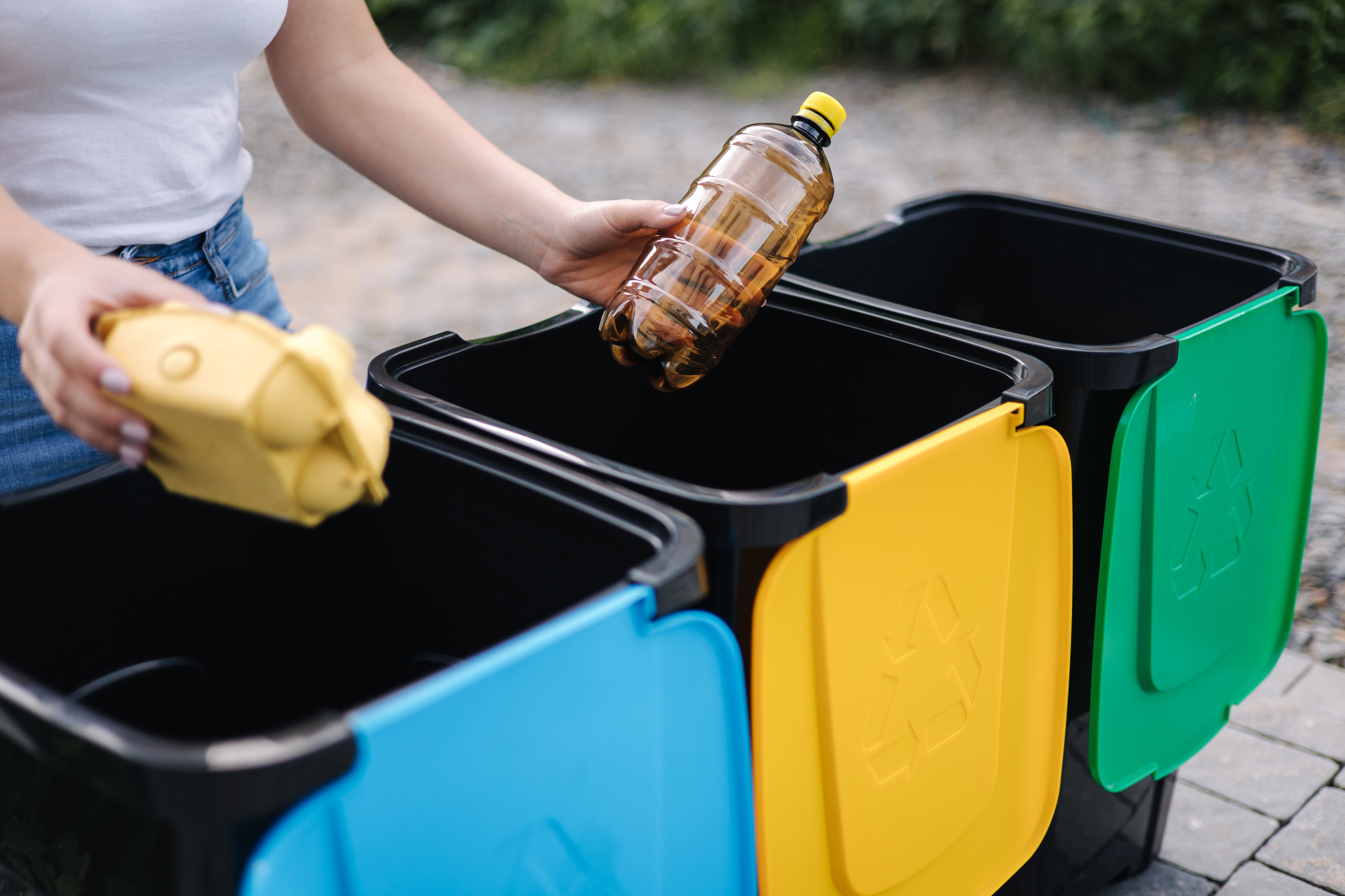 Mujer sosteniendo diferentes tipos de residuos, incluyendo botellas de plástico, representando la importancia del reciclaje en casa.