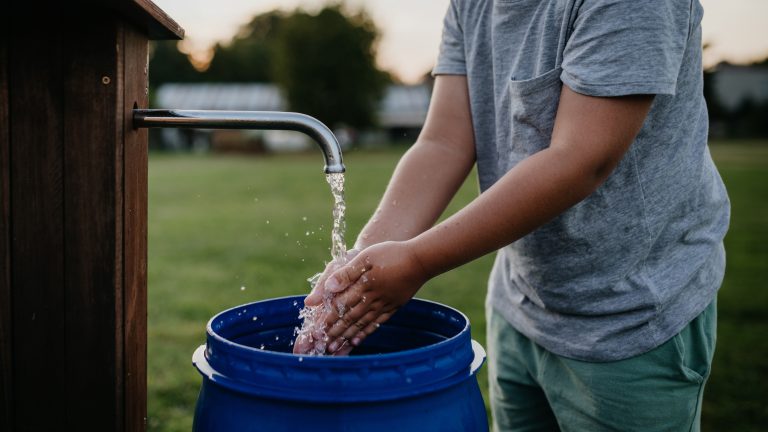 Niño lavándose las manos con agua extraída de un pozo en el jardín, ilustrando la importancia de reutilizar el agua de manera eficiente en el hogar.